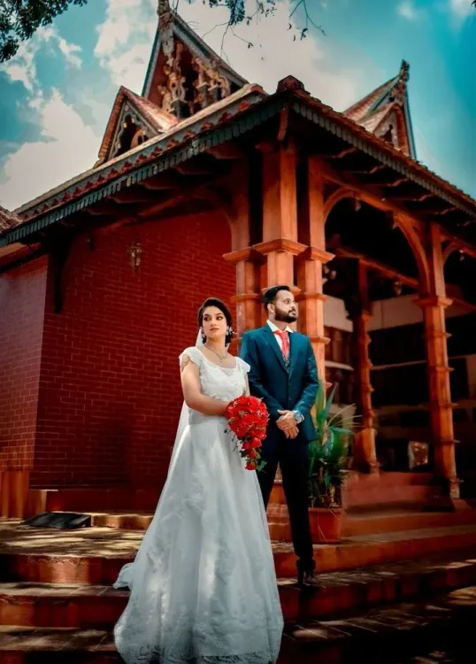 Bride and groom seated on the steps of a traditional Kerala-style building